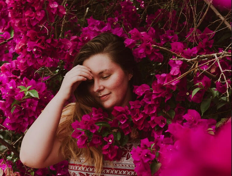 A white person with brown hair stands in a bougainvillea bush